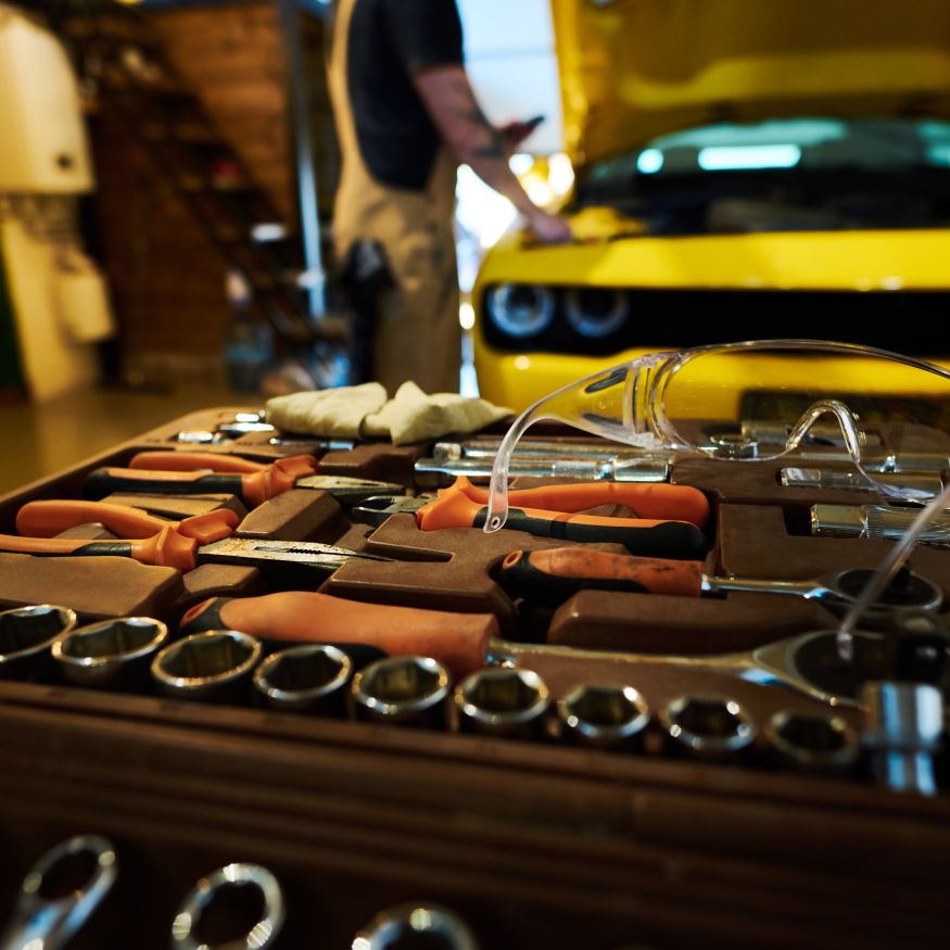 Protective eyeglasses on top of kit with spare parts and handtools for repair and checkup work of cars against repairman